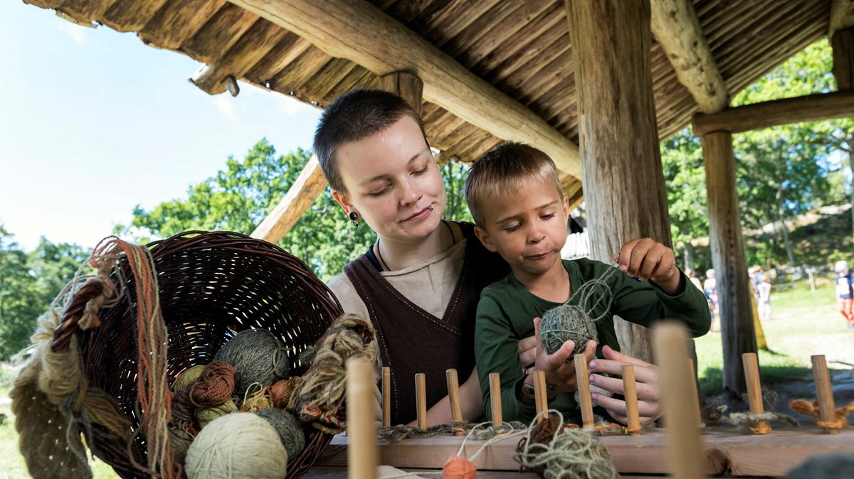 Ett barn som provar hantverk i bronsåldersgården.