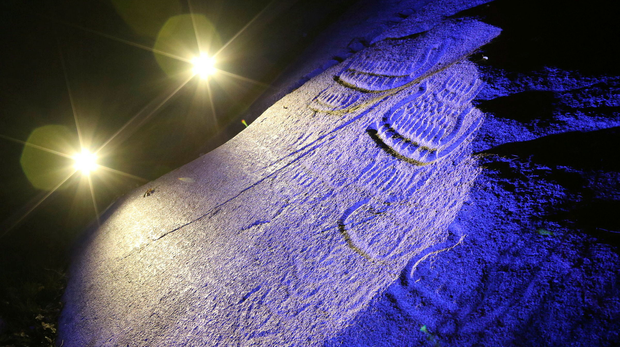 En berghäll med omålade ristningar belysta med släpljus i mörkret.