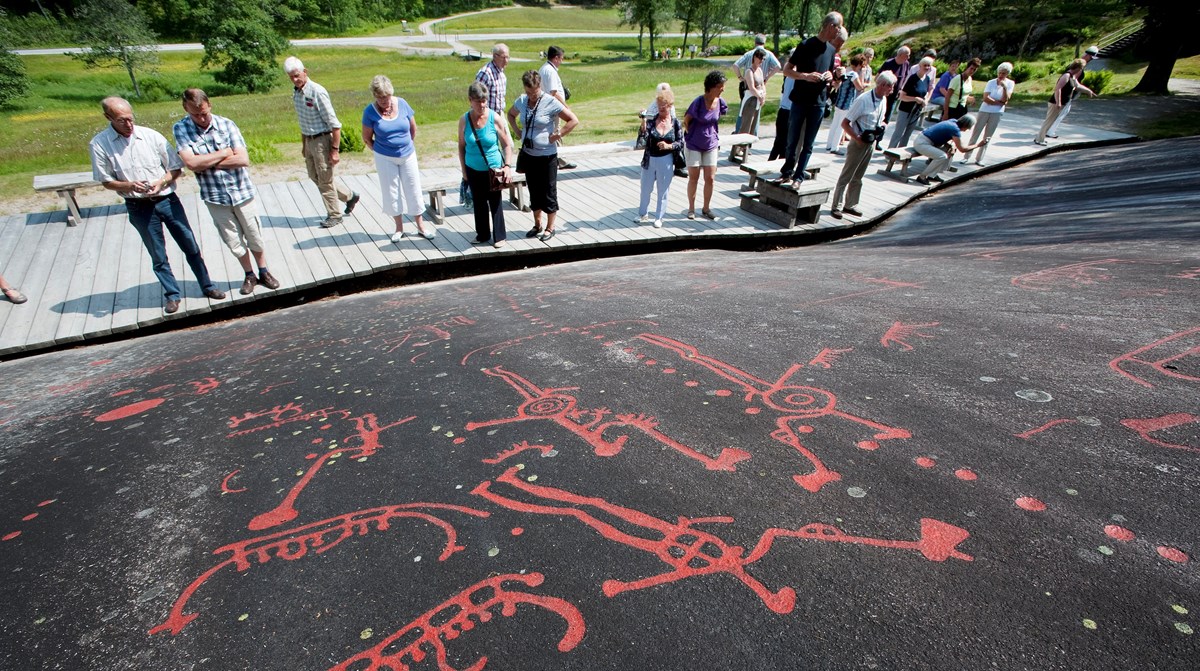 Vitlycke rock carvings and visitors viewing the panel.