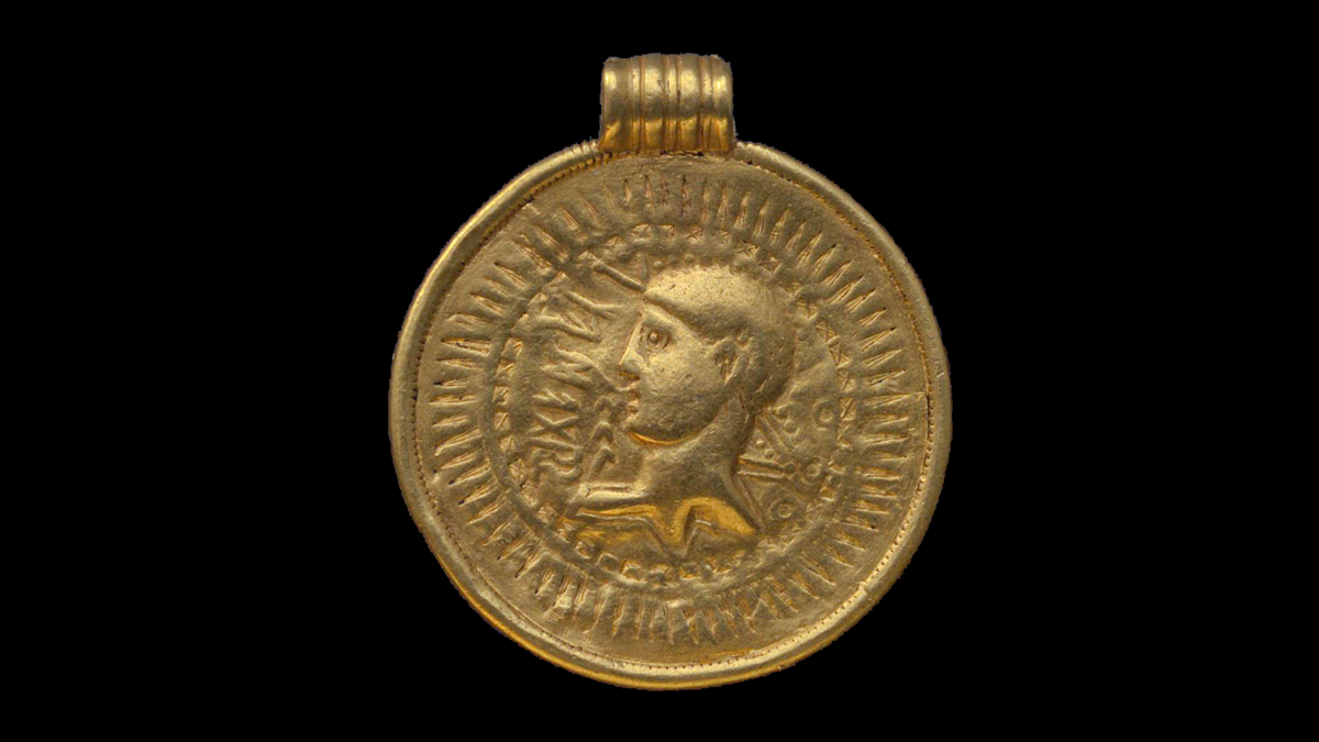 En medaljong i guld. På medaljongen en man i profil och några runor