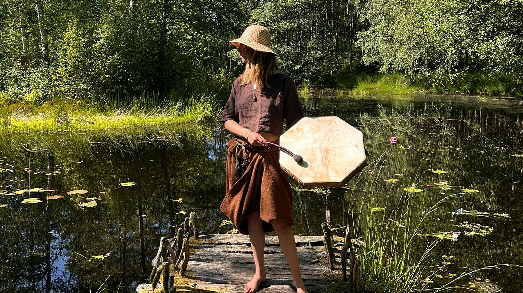 Kvinna klädd i bronsålderskläder hållandes i en trumma, vid offermosse, Vitlycke museum