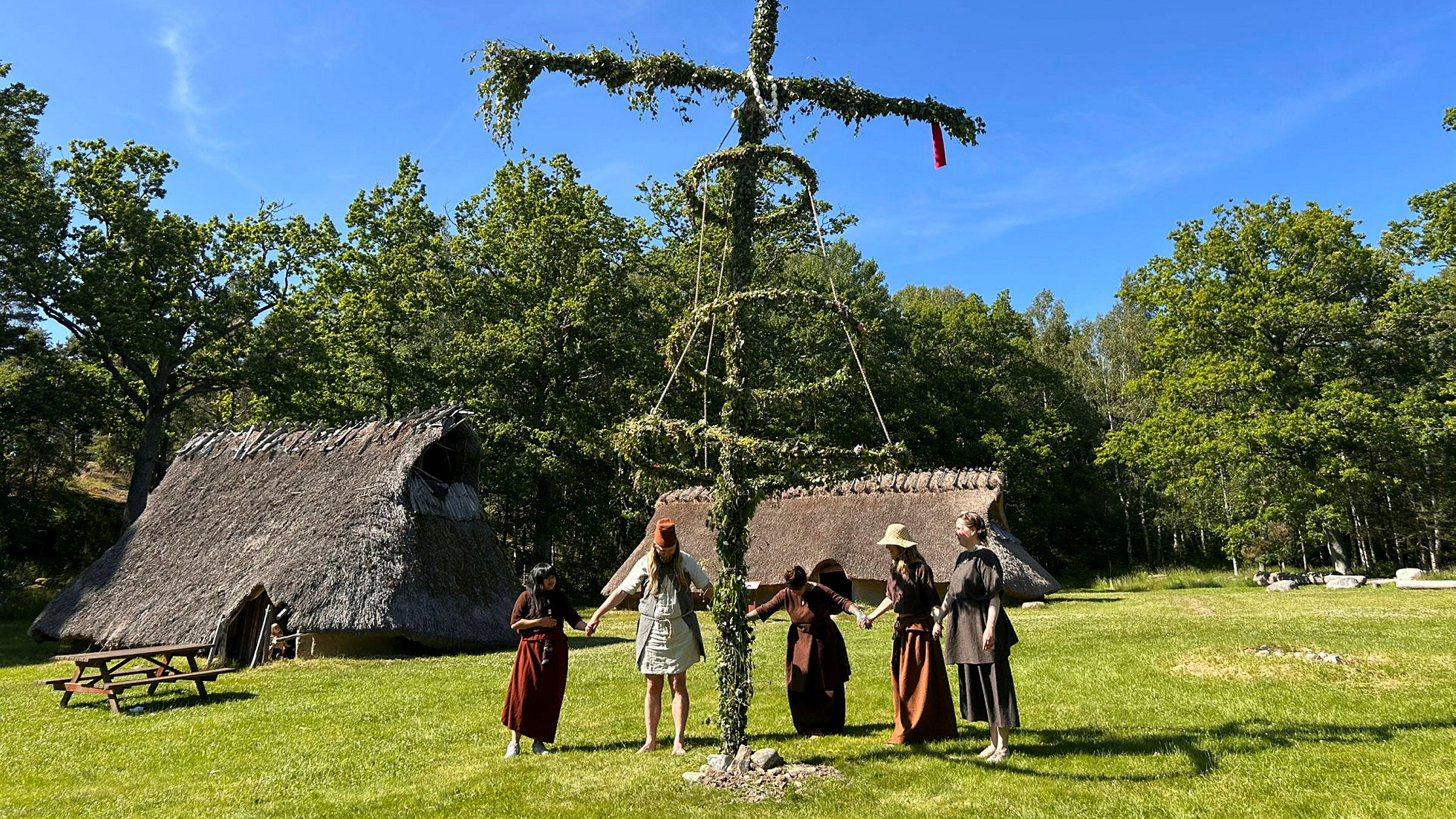 Mämnniskor i en ring dansar kring en midsommarstång