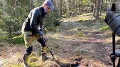 En man gräver står intill en häll och försöker blottlägga en hällristning.