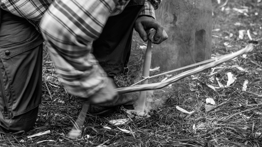 Eine Person entfacht mit einem Feuerbohrer ein urzeitliches Feuer