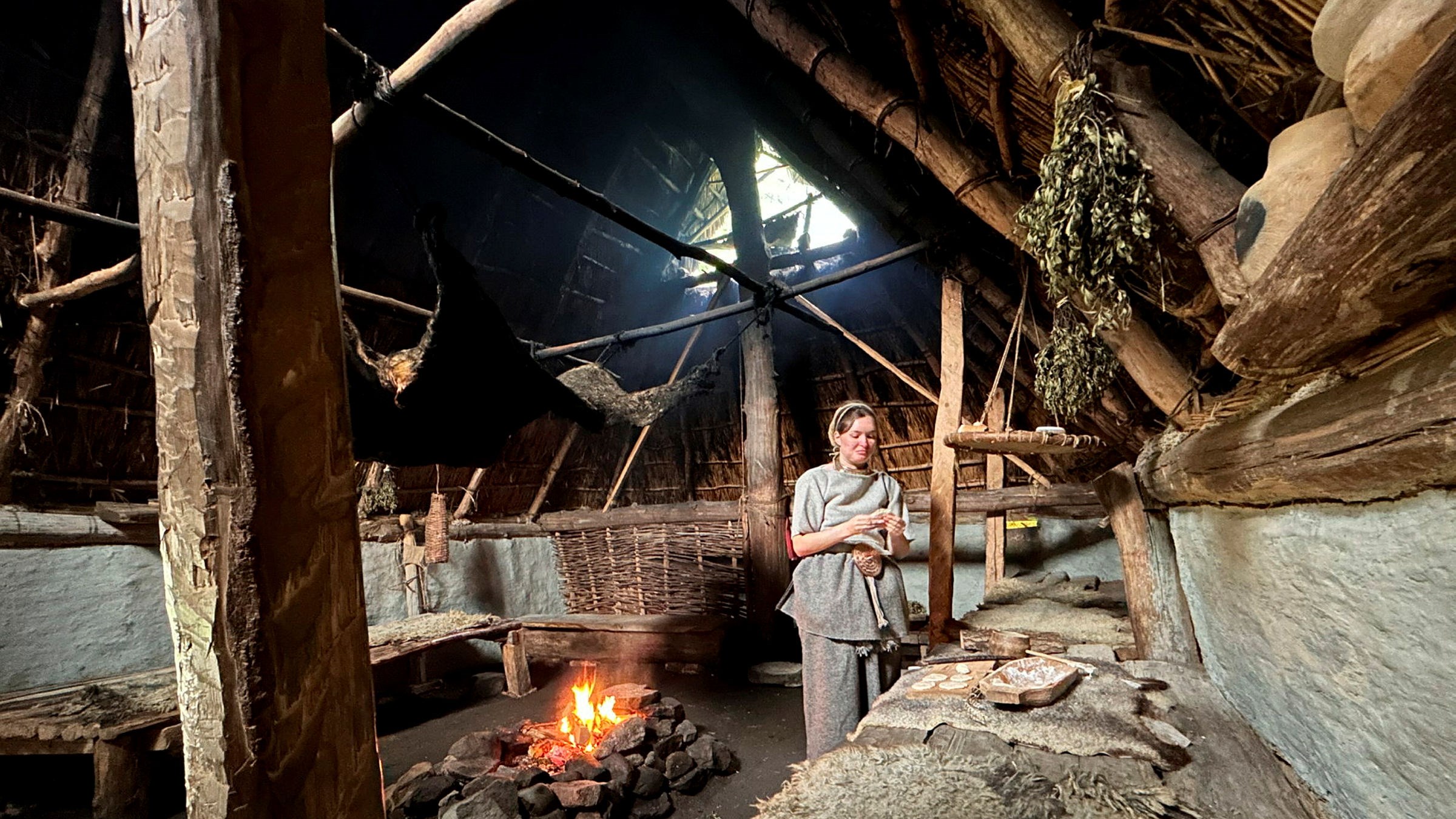 Gammalt hus med eldstad och kvinna klädd i ullkläder.