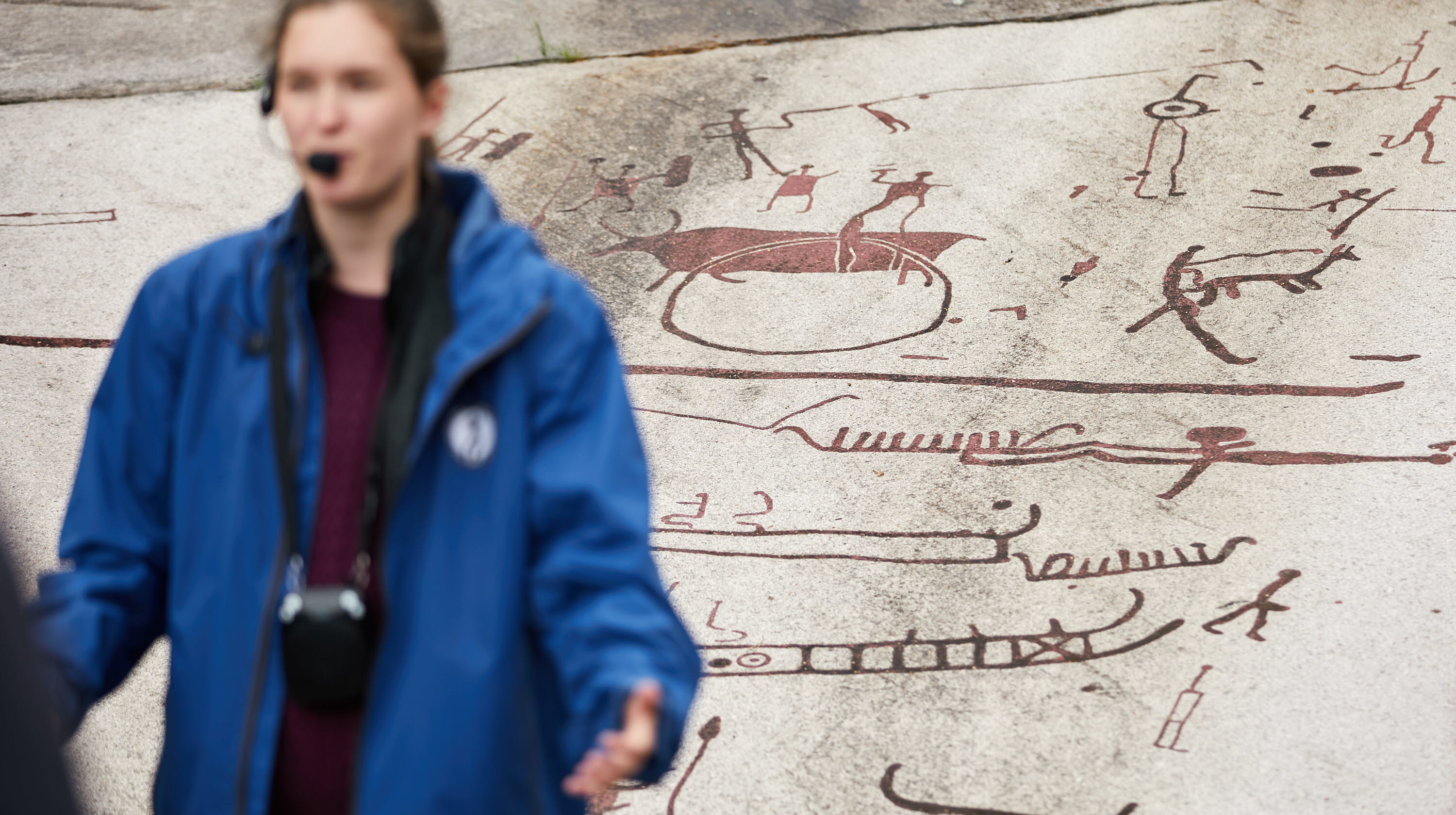 En guide med mikrofon framför hällristningar.